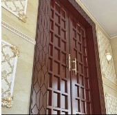 Elegant wooden interior door with intricate carvings and a golden handle, set within a beautifully decorated wall.